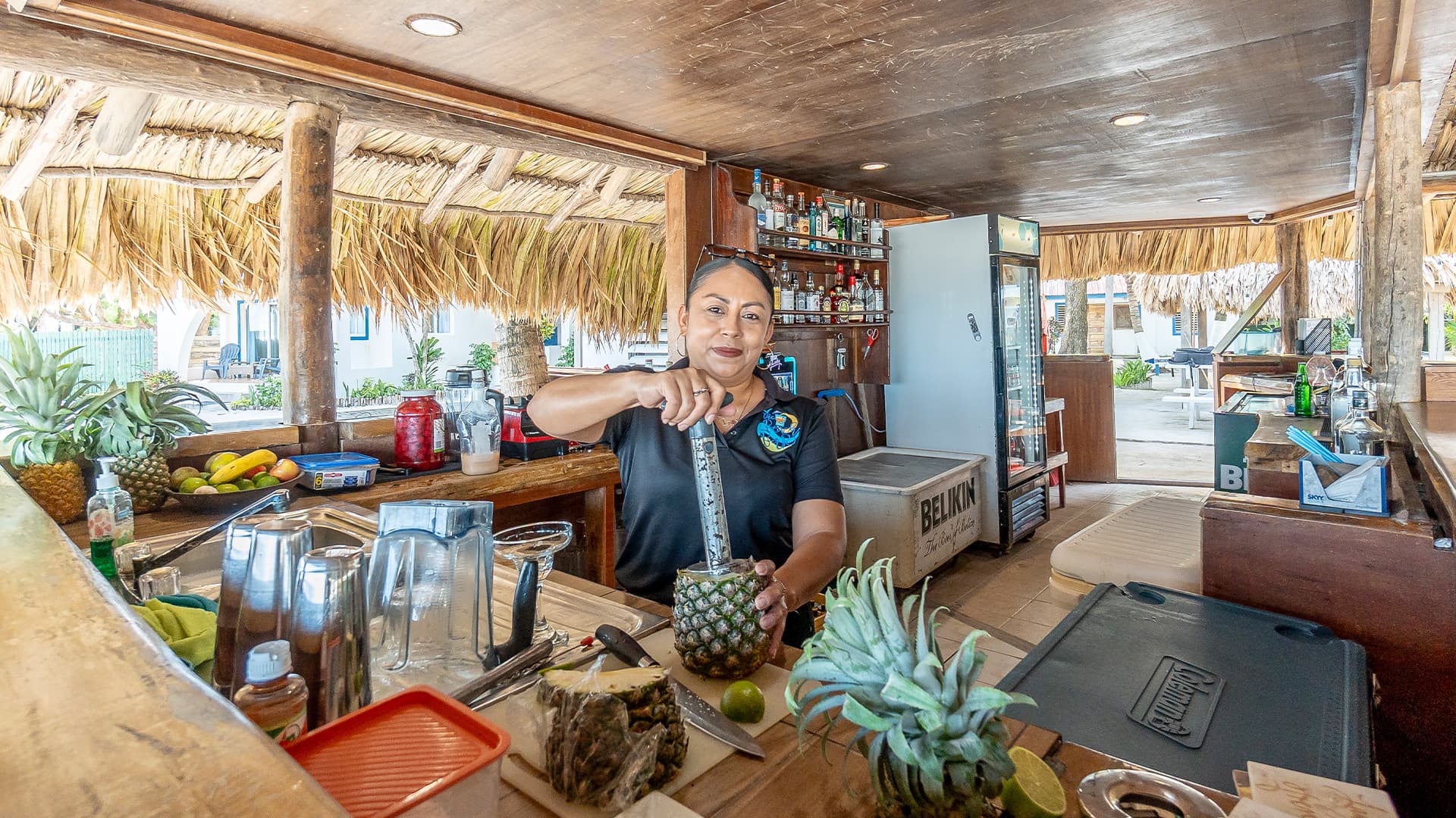 A bartender prepares a cocktail using a pineapple at a tropical bar.